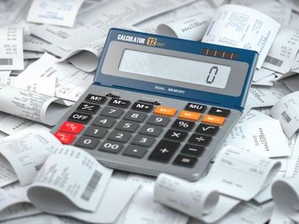 Hands with a calculator and printed spreadsheets on a desk.